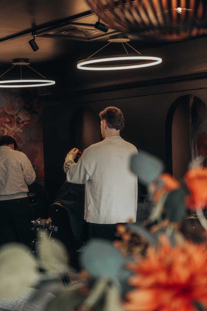 Barber working on a client at Monton Barbers in Beneden-Leeuwen, framed through soft foreground flowers